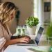 A woman intently focused on her laptop as she types out her thoughts.