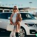 A well-dressed woman in designer clothing standing in front of her white Range Rover.