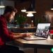 A man wearing a red flannel shirt working on designing a new website on his laptop.
