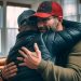 A father hugging his adult son in the living room.