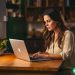 A brunette woman typing on her laptop at home.