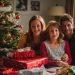 A happy middle class family smiling in front of the tree on Christmas morning.