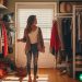 A young woman standing in her walk in closet, looking at the massive surplus of clothing she owns.