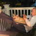 Male sitting on patio with his dog, scrolling on his phone next to a fire.